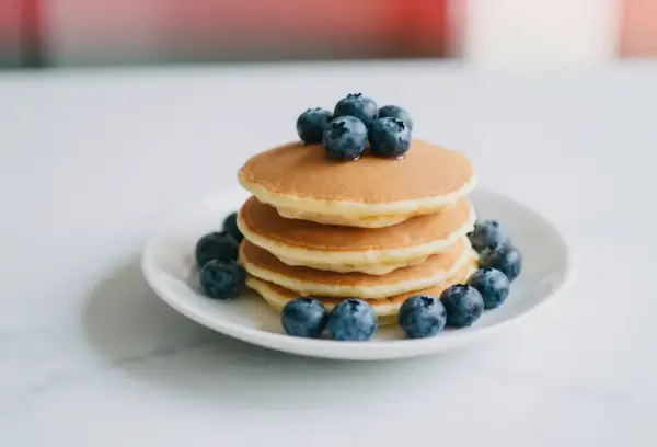 Stos puszystych pancakes z borówkami, ozdobiony świeżymi owocami. Idealne na słodkie śniadanie.