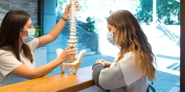 Fizjoterapeuta pokazuje pacjentce model kręgosłupa, wyjaśniając, jak wygląda dyskopatia lędźwiowa i przepuklina kręgosłupa.