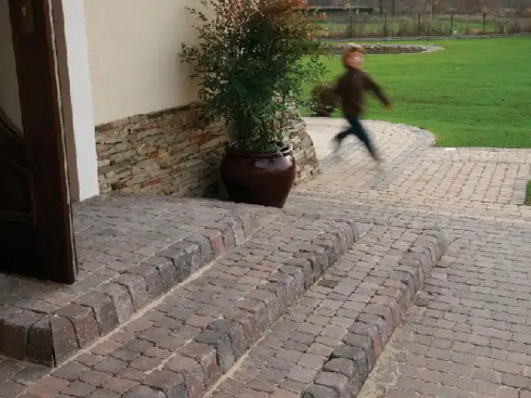 Schody z polbruku prowadzą do drzwi. W tle dziecko biegnie po trawniku.