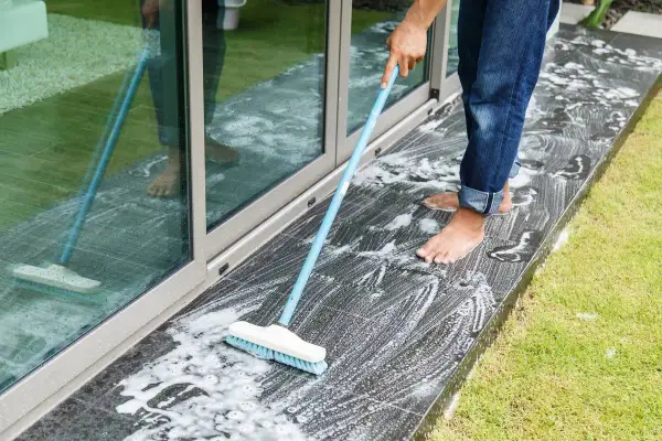 Persona a piedi nudi lava il marmo esterno annerito con una scopa e schiuma.