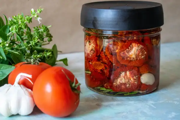 Glas mit eingelegten, sonnengetrockneten Tomaten, frischen Tomaten, Knoblauch und Basilikum. Perfekt für die Konservierung von Tomaten.
