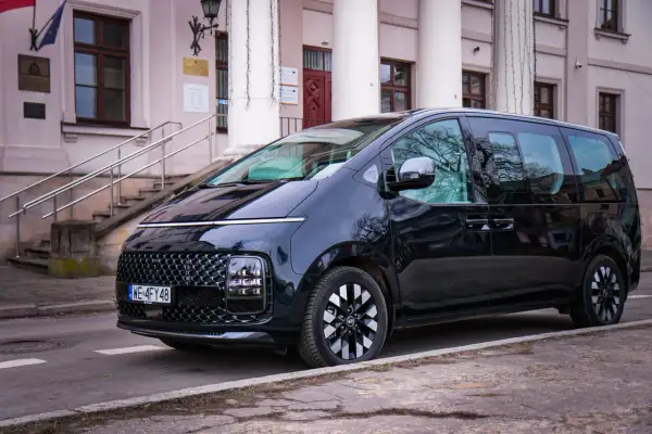 Czarny Hyundai Staria, nowoczesny van, zaparkowany przed budynkiem z kolumnami i schodami.