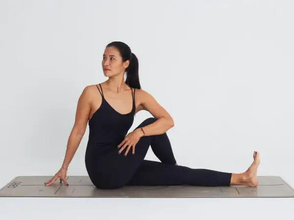 Mujer en postura de ardha matsyendrasana, girando el torso hacia la derecha, con la pierna izquierda flexionada y el pie derecho extendido.