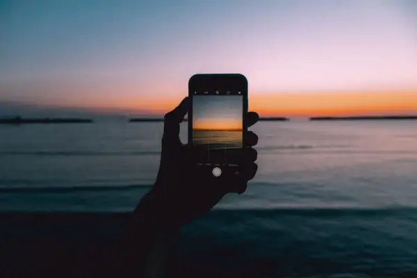 Dłoń trzyma smartfon, na którym widać piękny wschód i zachód słońca nad morzem.