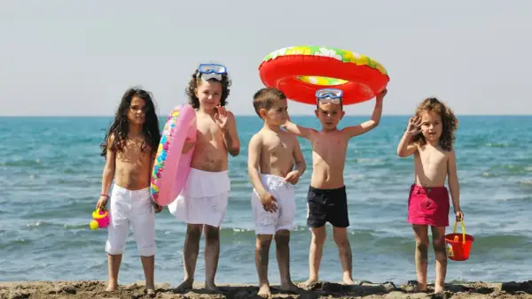 Piątka dzieci cieszy się wakacjami, gotowa na zabawy na plaży. Wśród nich są koła ratunkowe i wiaderko.