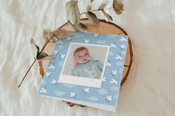 Carte de baptême avec photo d'un bébé, décorée de colombes et de nuages. Parfait pour trouver les mots pour baptême.