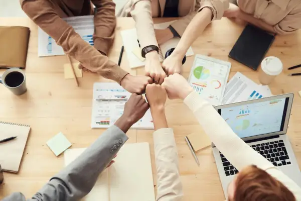 Equipo unido chocando puños sobre la mesa, simbolizando el logro de objetivos en la vida y metas compartidas.