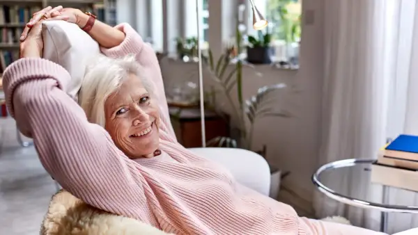 Vrolijke oudere vrouw ontspant in een fauteuil, genietend van rust. Een lat relatie elkaar weinig zien, maar ze vindt geluk in haar eigen gezelschap.