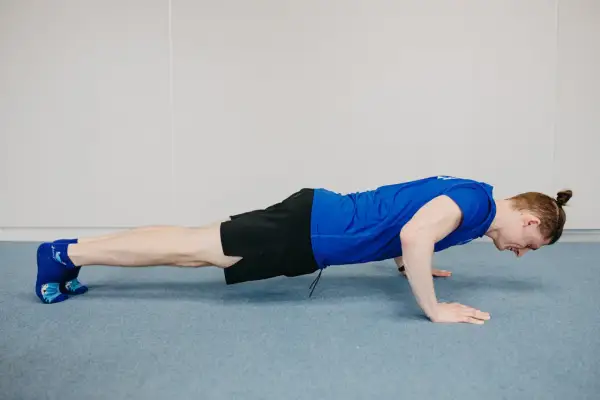 Mężczyzna wykonuje ćwiczenie diamond push ups, z dłońmi złączonymi pod klatką piersiową.