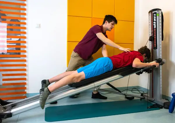 Fizjoterapeuta pomaga pacjentowi w ćwiczeniach na ławce rehabilitacyjnej. Skupiają się na rehabilitacji ortopedycznej, by odzyskać sprawność.