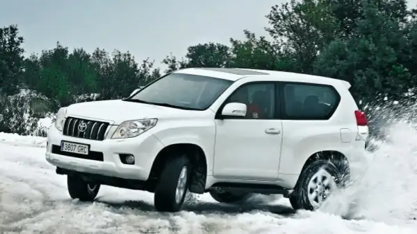 Toyota Land Cruiser 3.0 D4D 163 CV ficha técnica: un blanco todoterreno navega por nieve y agua, demostrando su potencia.