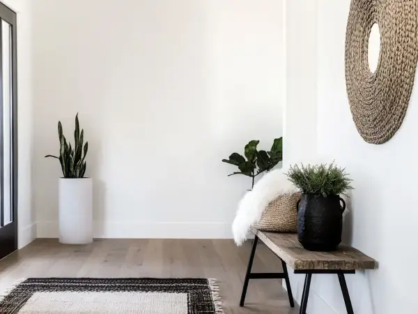 Przytulny przedpokój w stylu boho z drewnianą ławką, plecionym lustrem i zielonymi roślinami.