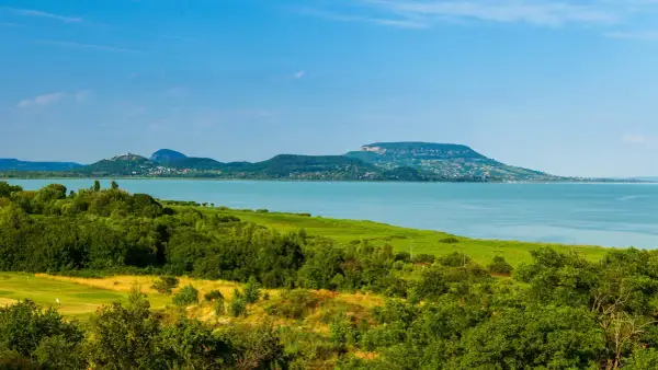 Malowniczy krajobraz z jeziorem Balaton na Węgrzech, zielone wzgórza i błękitne niebo.