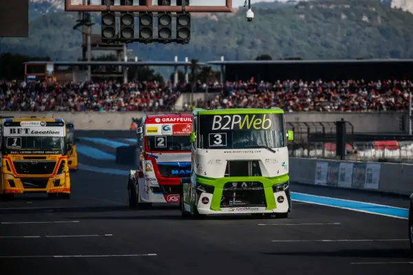 Des camions de course s'affrontent lors du **grand prix camion Castellet**. Le camion n°3, vert et blanc, mène la course devant le n°2 rouge et blanc.