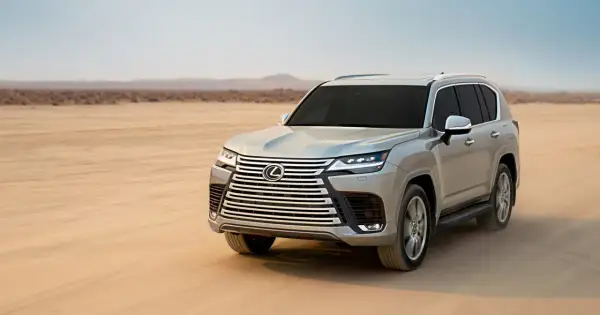 Srebrny Lexus LX 600 przemierza pustynię, unosząc tumany piasku.