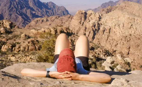 Une personne se repose sur un rocher, les mains derrière la tête, admirant le paysage désertique lors d'un trek en Jordanie.