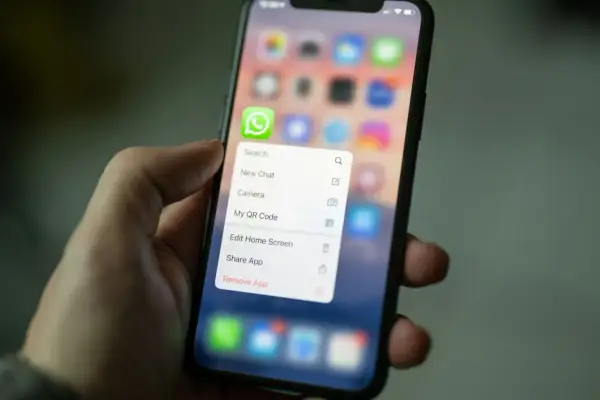 Dłoń trzyma smartfon z menu aplikacji WhatsApp. Można tu znaleźć opcję "Kopia zapasowa WhatsApp" (choć nie jest widoczna na ekranie, jest to kontekst).