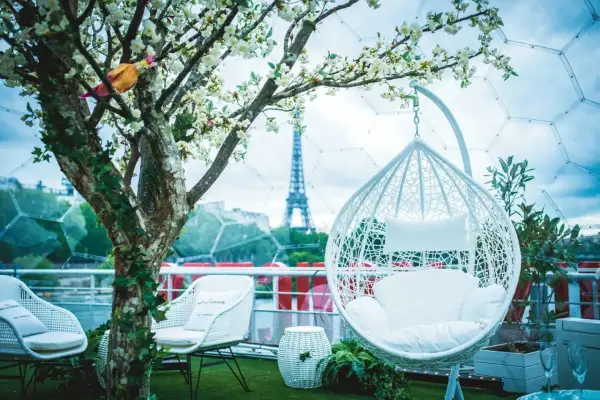 Un décor romantique pour un speed dating Paris, avec la Tour Eiffel en arrière-plan. Fauteuils blancs, balancelle et arbre fleuri créent une ambiance féerique.
