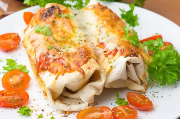 Dwa zapieczone burrito z kurczakiem, polane ciągnącym się serem, podane z pomidorkami koktajlowymi i natką pietruszki.