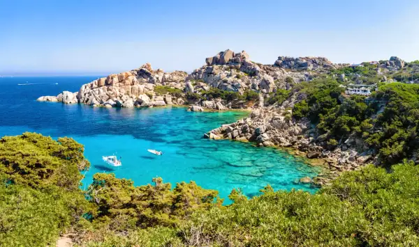 Türkisblaues Meer, Felsenbuchten und grüne Macchia – diese Szenerie verspricht die beste Reisezeit Sardinien. Kleine Boote schaukeln im Wasser.