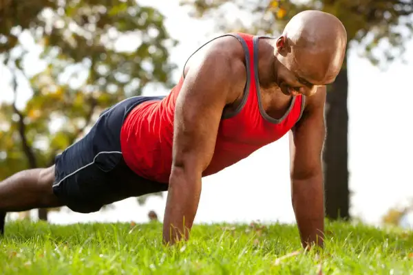 Homme chauve en tenue de sport faisant un exercice bras sur l'herbe.