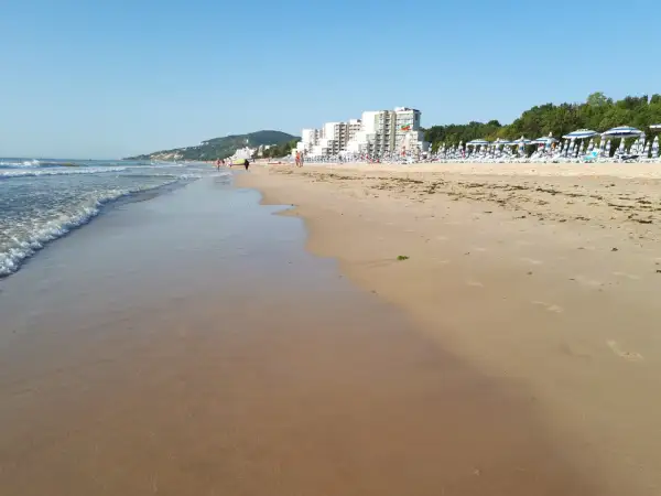 Piękna plaża w Albena Bułgaria. Fale obmywają piaszczysty brzeg, a w oddali widać hotele i rzędy parasoli.