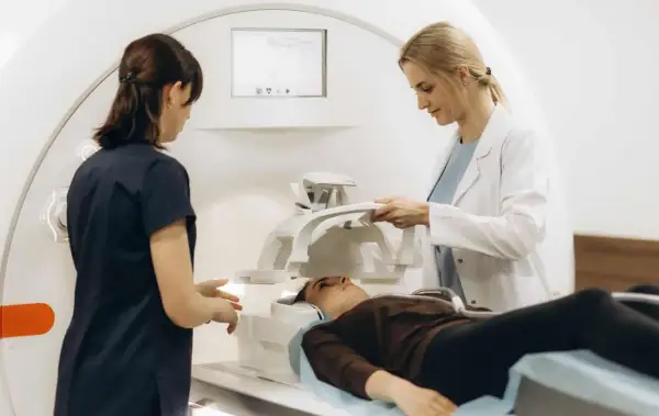 Zwei medizinische Fachkräfte bereiten eine Patientin für radiologische Untersuchungen vor. Sie liegt auf einer Liege neben einem MRT-Gerät.
