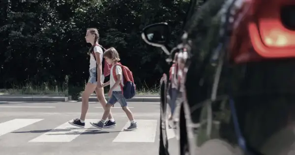 Dwoje dzieci, pieszy na pasach, z plecakami przechodzi przez ulicę.