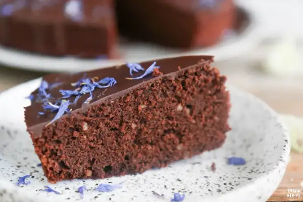 Ein Stück saftiger schokokuchen ohne zucker, garniert mit blauen Kornblumenblättern auf einem Teller.