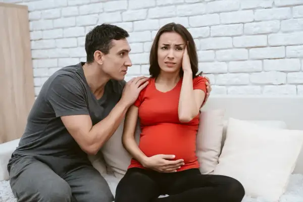 Uomo consola donna incinta con mal di testa, preoccupati per la crisi di coppia in gravidanza.
