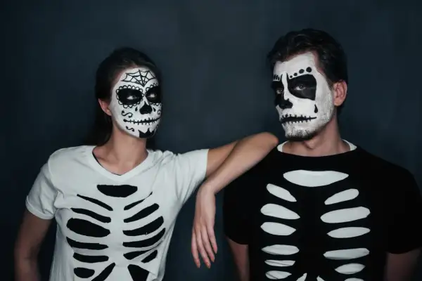 Coppia con trucco da teschio e magliette fai da te a tema scheletro, perfetti per costumi Halloween uomo e donna.