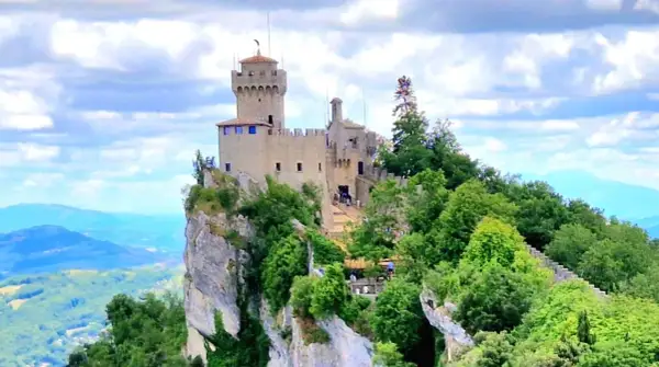 San Marino: en medeltida borg tronar på en klippavsats, omgiven av grönskande träd och med en vidsträckt vy över kullar och berg.
