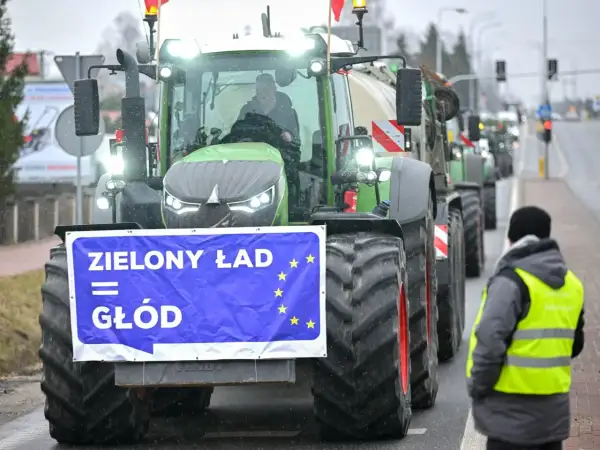 Traktor z banerem "Zielony Ład = Głód" i flagą UE, w tle protestujący rolnicy.