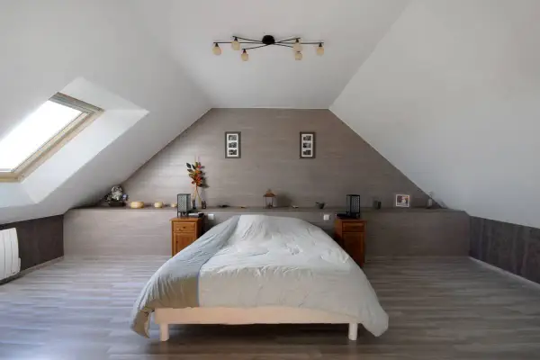 Douillette chambre mansardée avec un grand lit, une fenêtre de toit et une décoration sobre.