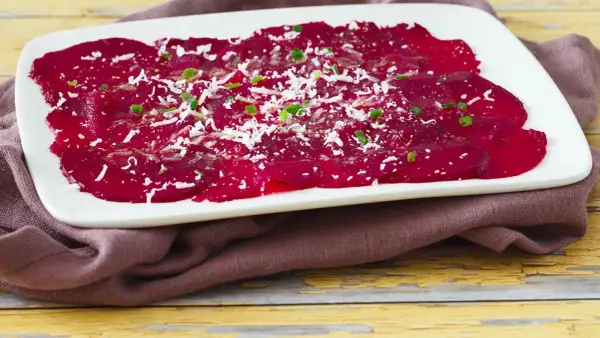 Rote Bete Carpaccio, hauchdünn geschnitten und mit Parmesan und Schnittlauch bestreut, auf einem weißen Teller.