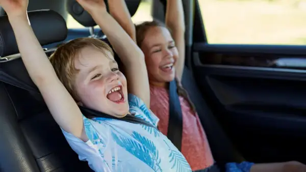 Niños emocionados en el coche, con los brazos en alto. Parecen haber alcanzado la altura mínima para no usar silla en el coche.