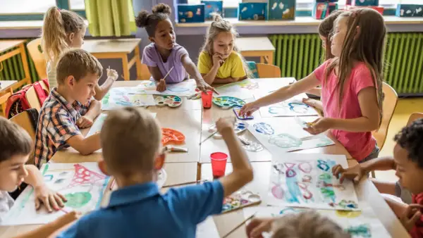Niños y niñas disfrutan del arte en infantil, pintando con acuarelas y pinceles en una clase creativa.