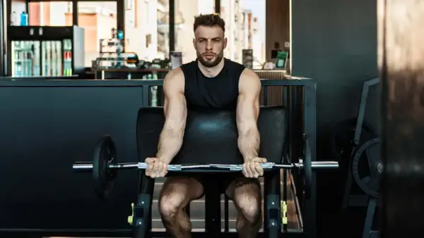 Mann trainiert Bizeps mit Langhantel im Fitnessstudio. Calisthenics-Liebhaber baut Muskeln auf.
