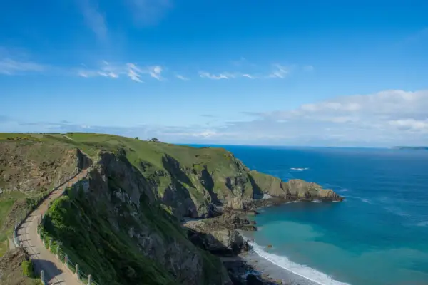 Chemin côtier verdoyant sur les falaises de Jersey, idéal pour visiter Jersey à pied. Mer bleue et ciel clair.