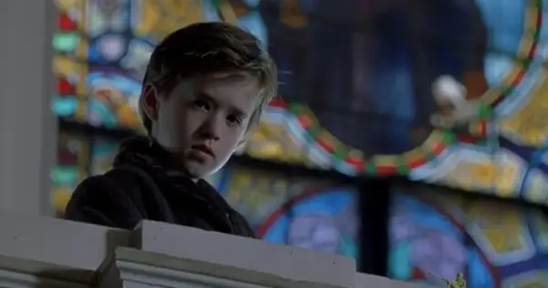 Chłopiec z filmu "Szósty zmysł" Haley Joel Osment w kościele, za nim witraż.
