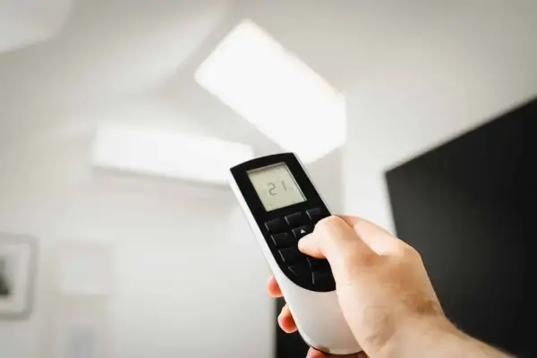 Main tenant ajuste la température de son climatiseur PAC split à 21°C avec la télécommande.