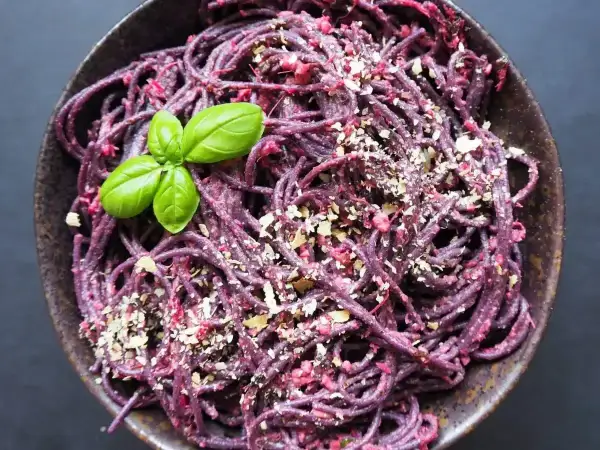 Fioletowy makaron z pesto z buraków, posypany orzechami i udekorowany listkami bazylii.
