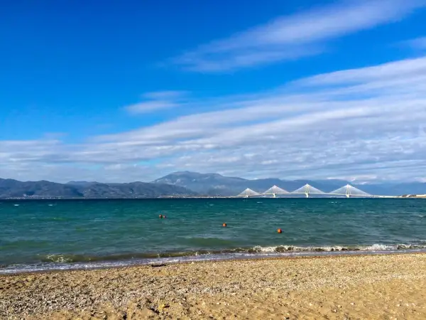 Spokojne morze i plaża w Grecji w styczniu. W oddali widać most i góry.