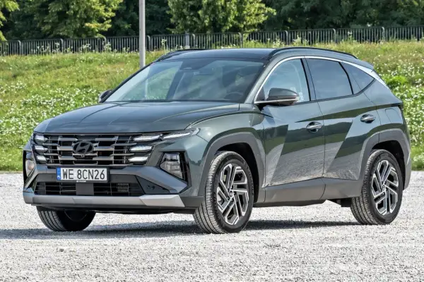 Nowy, tani SUV Hyundai Tucson w ciemnozielonym kolorze, zaparkowany na żwirowej drodze.