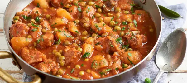 Un saporito spezzatino di vitello con piselli e patate, cotto in un sugo rosso e guarnito con prezzemolo fresco.