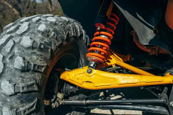 Gros plan sur la jambe de force voiture, avec son amortisseur orange vif et son pneu tout-terrain. Le bras de suspension jaune vif est prêt pour l'aventure.