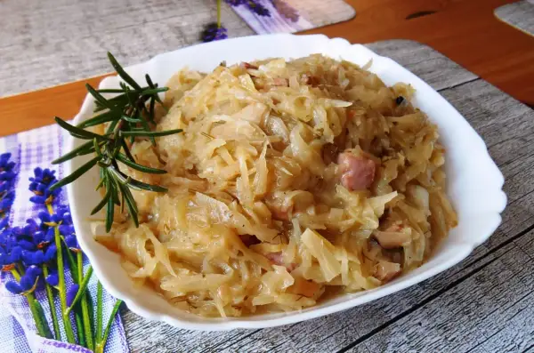 Pyszna kapusta zasmażana z boczkiem, podana na białym talerzu, ozdobiona gałązką rozmarynu.