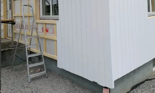 Byggarbetsplats där man valt att kombinera liggande och stående panel på husfasaden. En stege står redo.