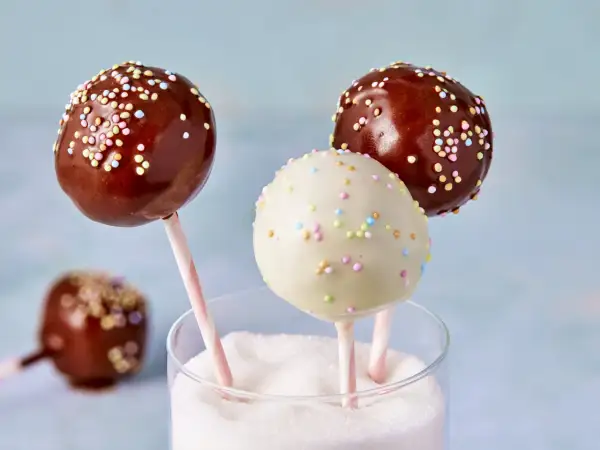Leckere cake pops aus kuchenresten, verziert mit bunten Streuseln, stecken in einem Glas voller Zucker.