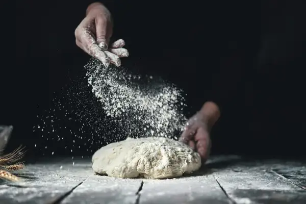 Händer strör mjöl över en deg. Det ser ut som en svensk hemmabakare som förbereder sitt bröd med fint **bread flour svenska**.